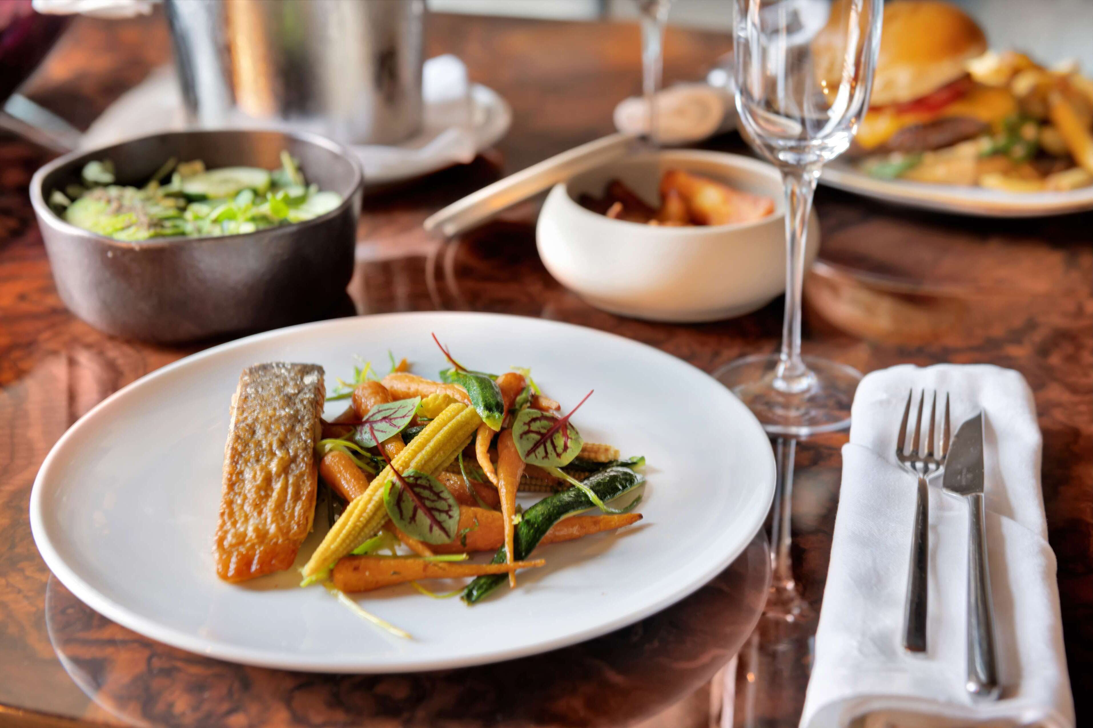 A dining table with a plate of food, a glass of wine, and a bowl of salad.
