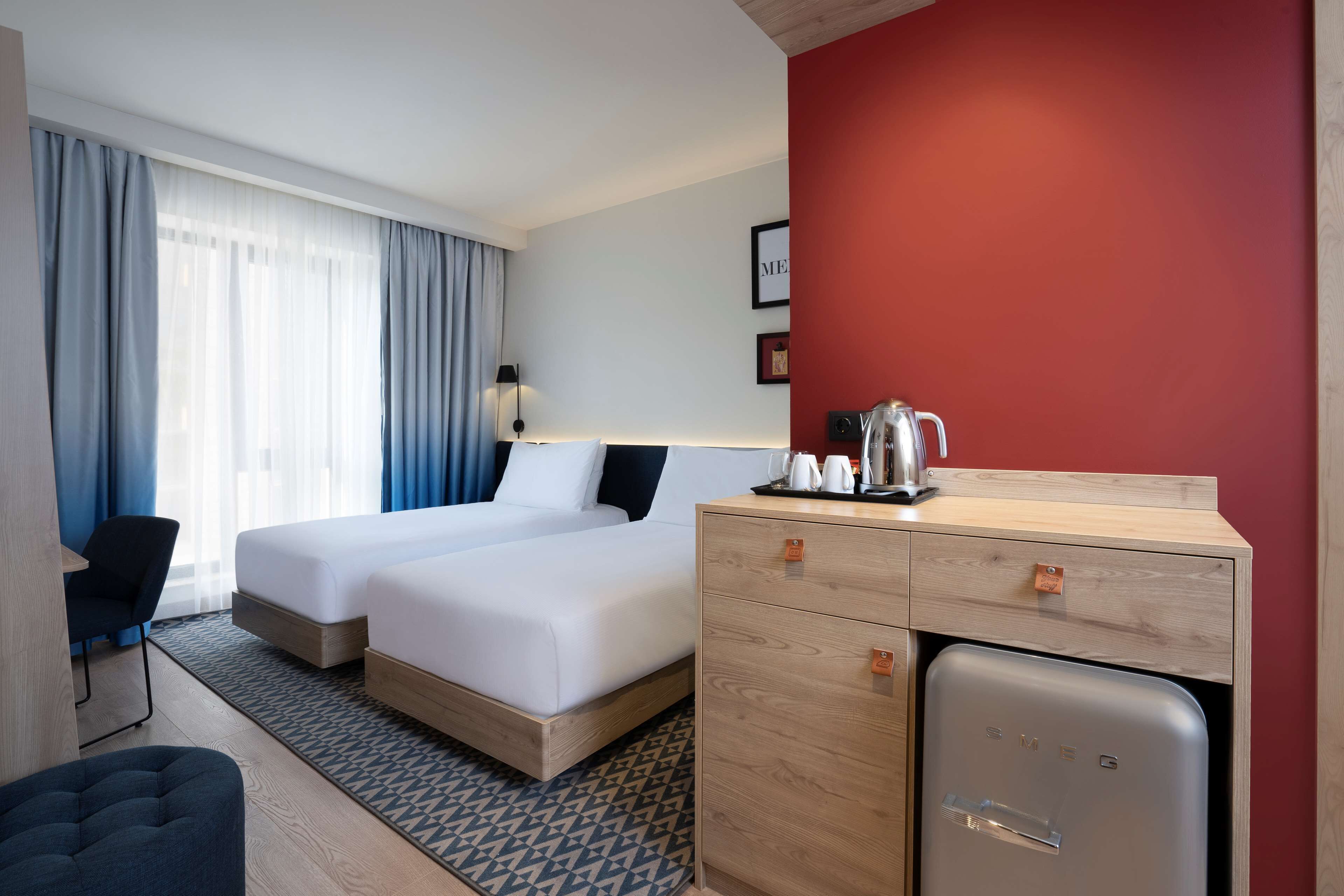 A hotel room with two beds, a desk with a refrigerator, and a chair.