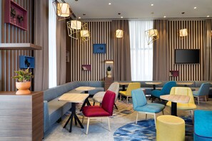 A modern lounge area with striped walls, multiple seating options including sofas and chairs, and a flat-screen TV mounted on the wall. - Hampton by Hilton Tashkent (Tashkent)