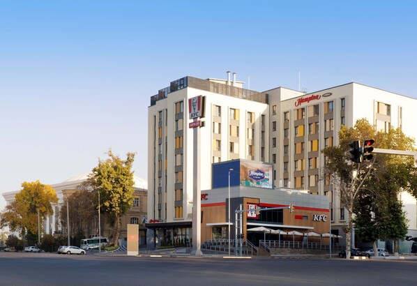 A multi-story building with KFC and Hampton Inn signage, featuring a modern architectural design with a flat roof and large windows. - Hampton by Hilton Tashkent (Tashkent)