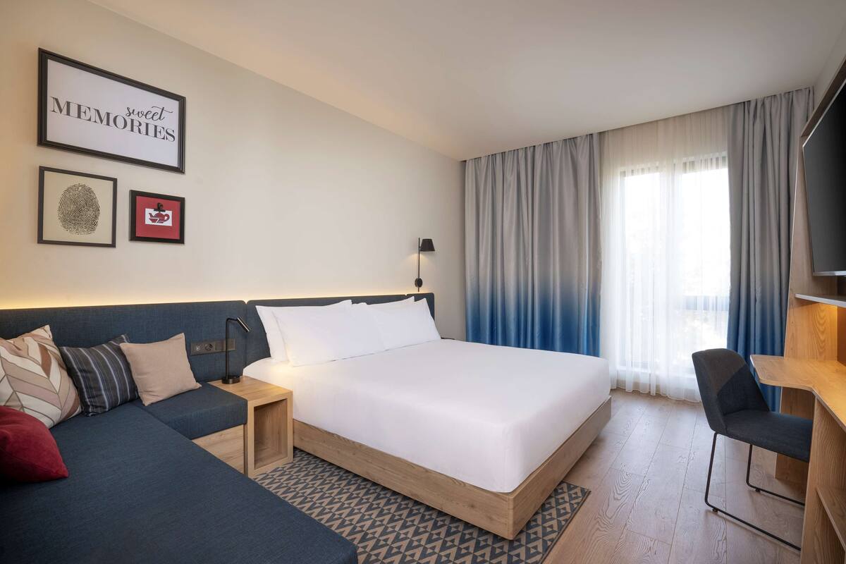 A modern hotel room with a large bed, a sofa, a desk, and a TV.