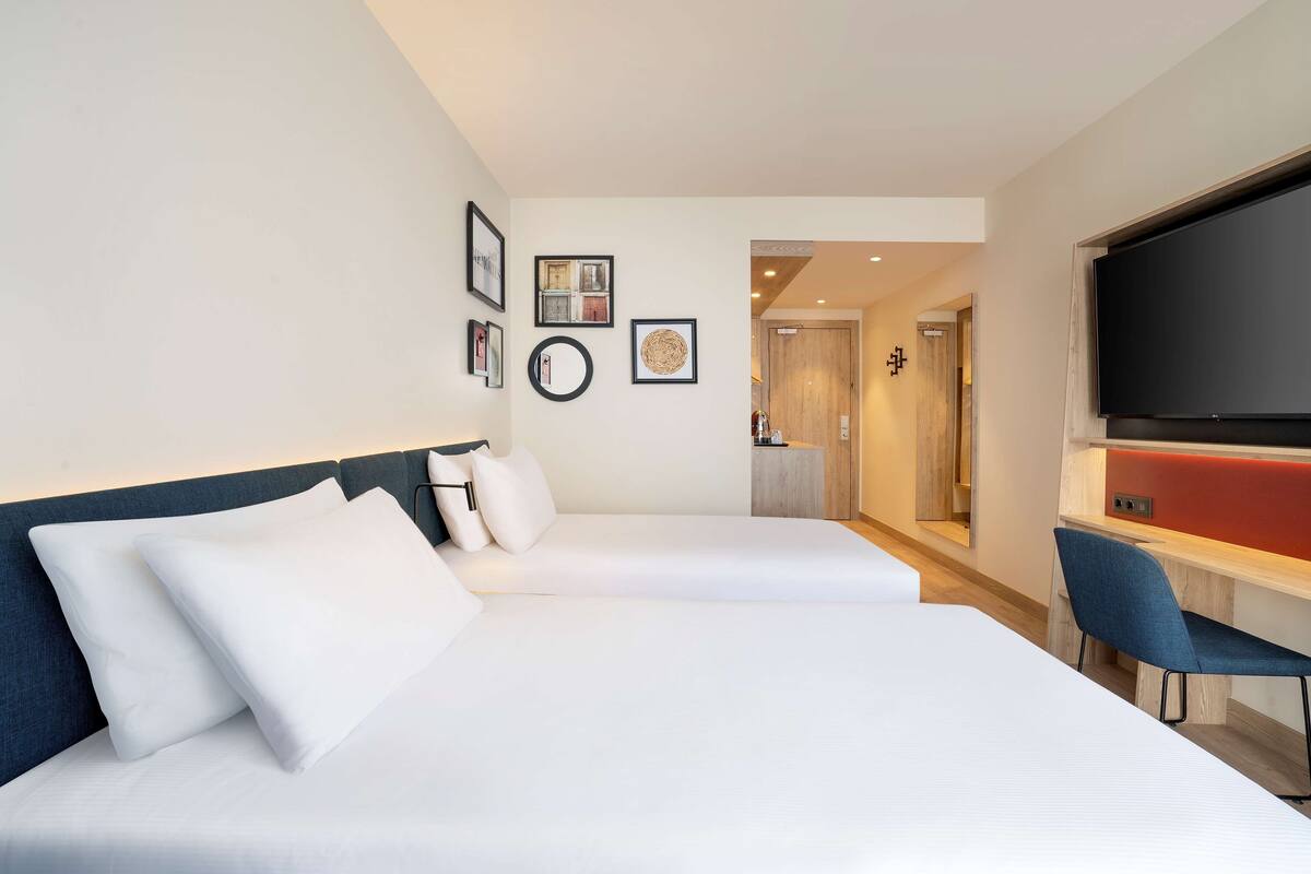 A hotel room with two beds, a TV, and a desk with a chair.
