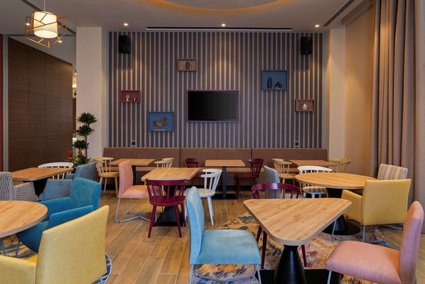 A modern restaurant interior with striped wall decor, a flat-screen TV, and a variety of colorful seating options.