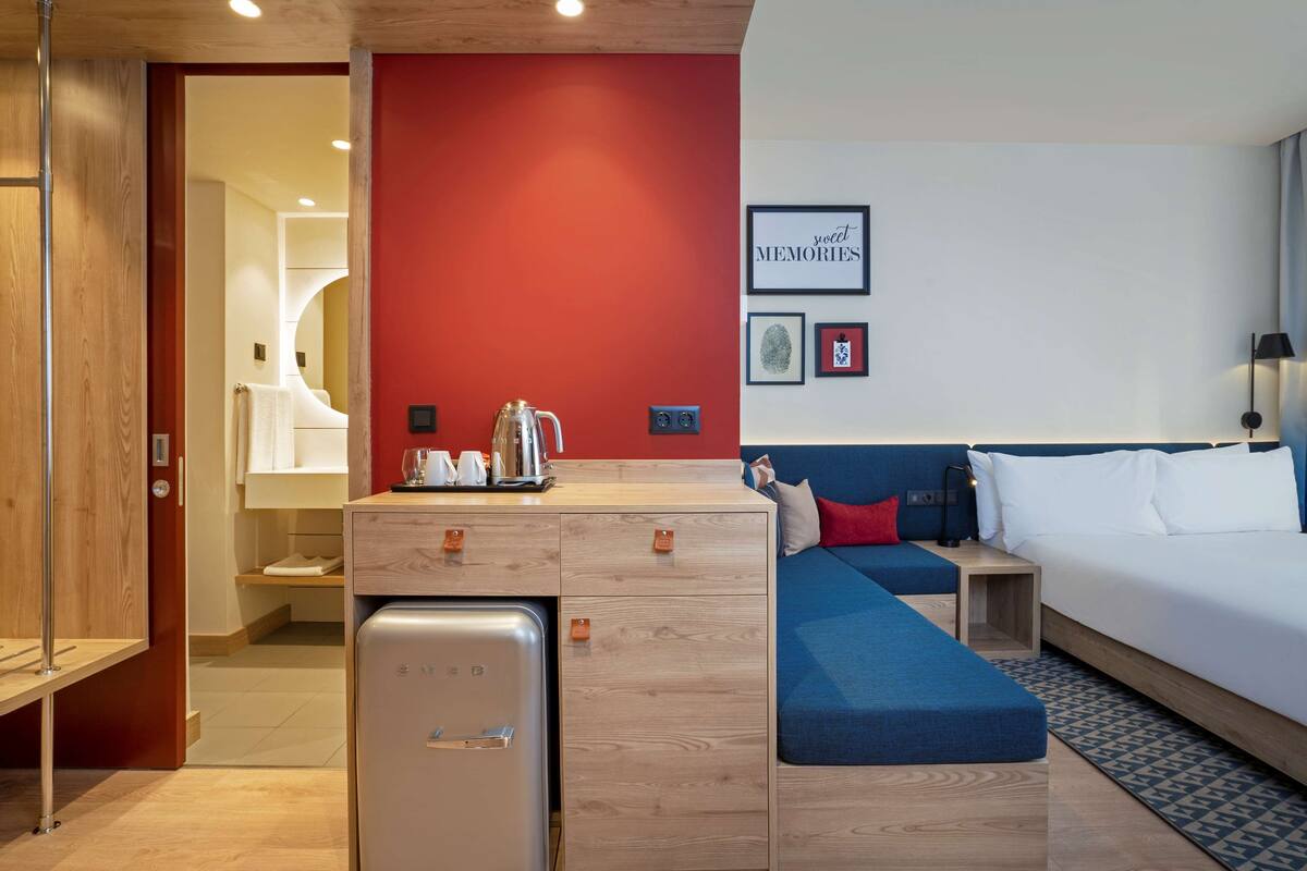 A compact hotel room with a kitchenette, a sofa, a bed, and a small table.