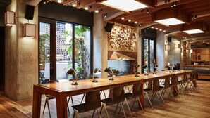 A long wooden table with chairs, a large window with plants, and a modern ceiling design. - Ace Hotel Brooklyn (Brooklyn)