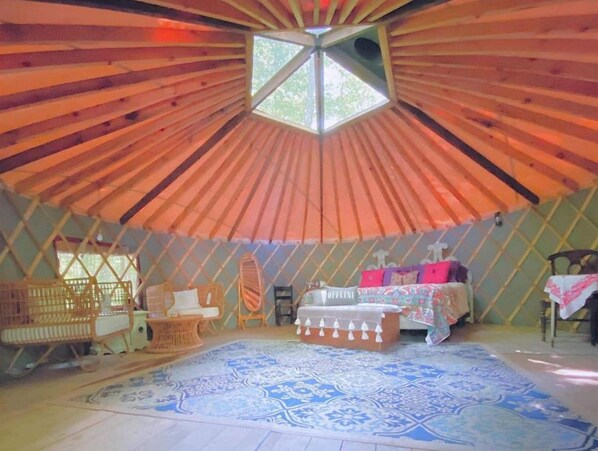 A yurt with a central skylight, a bed with a 'OFFLINE' sign, a woven chair, and a patterned rug.