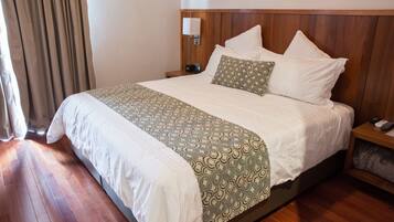 A neatly made bed with a patterned bedspread, a bedside table with a lamp, and a nightstand with a remote control.