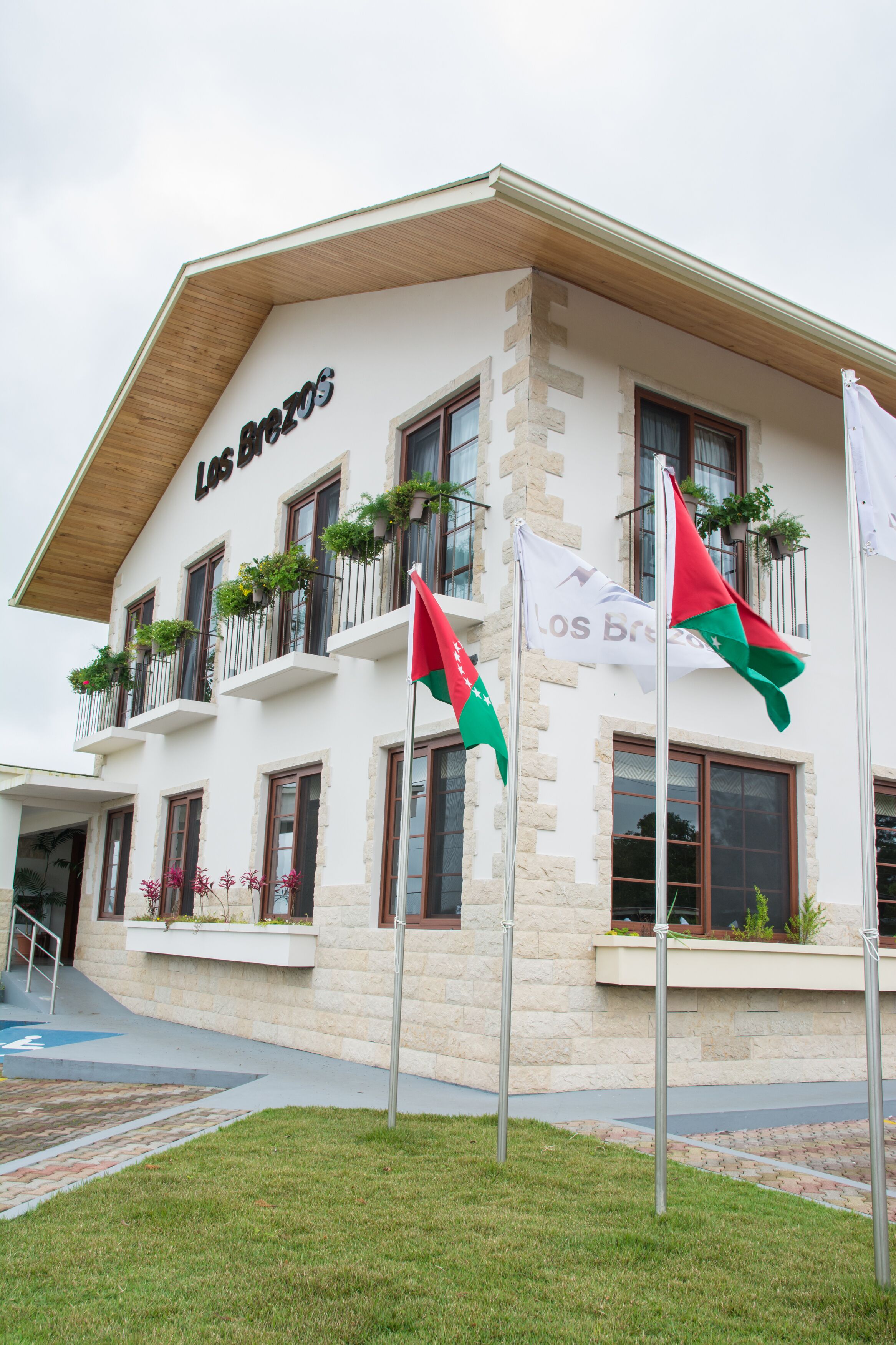 A hotel with a white facade, balconies with plants, and flags.