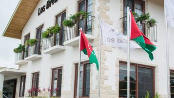 A hotel with a white facade, balconies with plants, and flags.