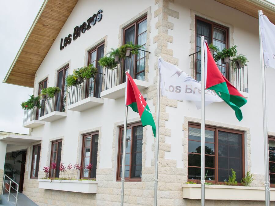 A hotel with a white facade, balconies with plants, and flags.