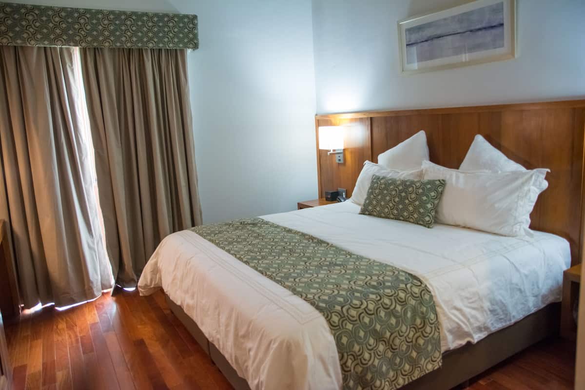 A neatly made bed with a patterned bedspread, a wooden headboard, and a bedside lamp.