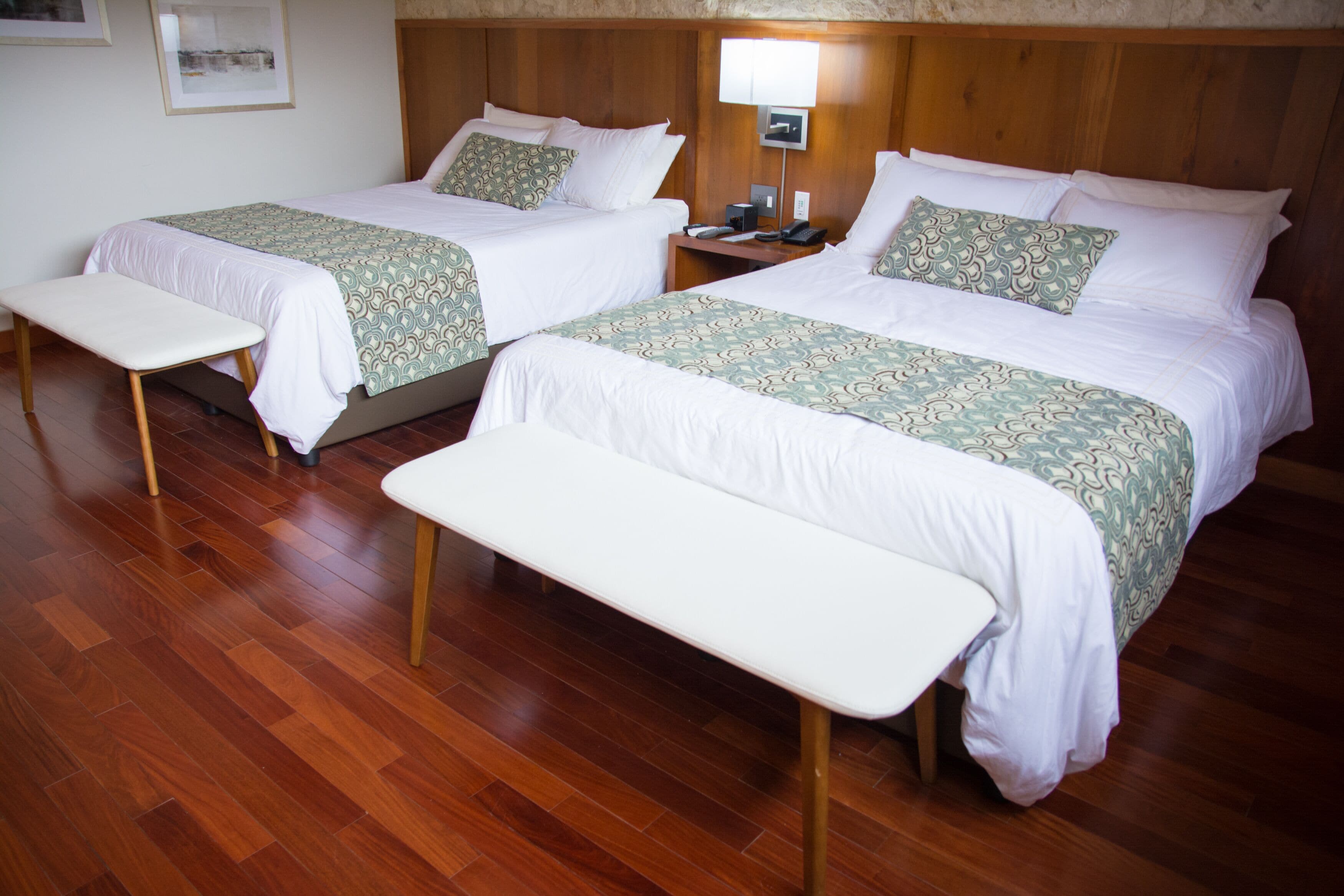 A hotel room with two beds, a nightstand, a desk, and a bench.