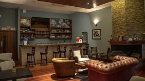 A bar area with a counter, bar stools, and a fireplace. There are leather sofas and a table with chairs. - Los Brezos Boutique Hotel (Volcan)