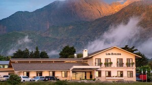 A building named "Los Brezos" with a parking area in front, surrounded by mountains and some vegetation. - Los Brezos Boutique Hotel (Volcan)