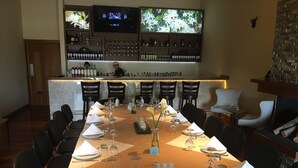 A restaurant with a long table set for a meal, a bar with various bottles, and a television screen above the bar. - Los Brezos Boutique Hotel (Volcan)