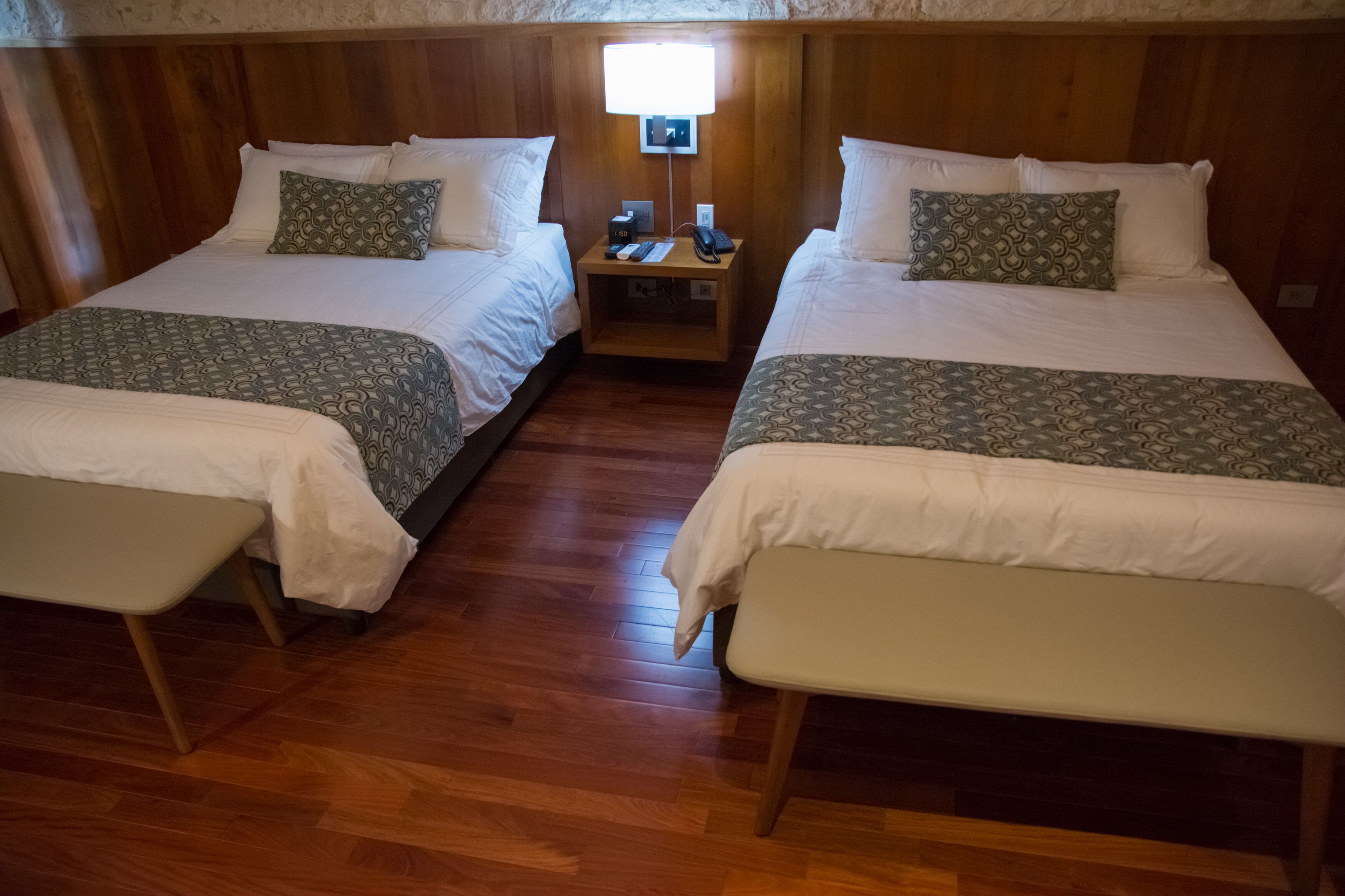 Habitación con dos camas, cada una con una colcha estampada y almohadas a juego, una mesita de noche con lámpara y suelo de madera.