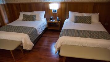 Habitación con dos camas, cada una con una colcha estampada y almohadas a juego, una mesita de noche con lámpara y suelo de madera.