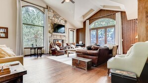 A spacious living room with a stone fireplace, leather furniture, and large windows offering views of the outdoors. - 2-2122 Vermont Road (Vail)