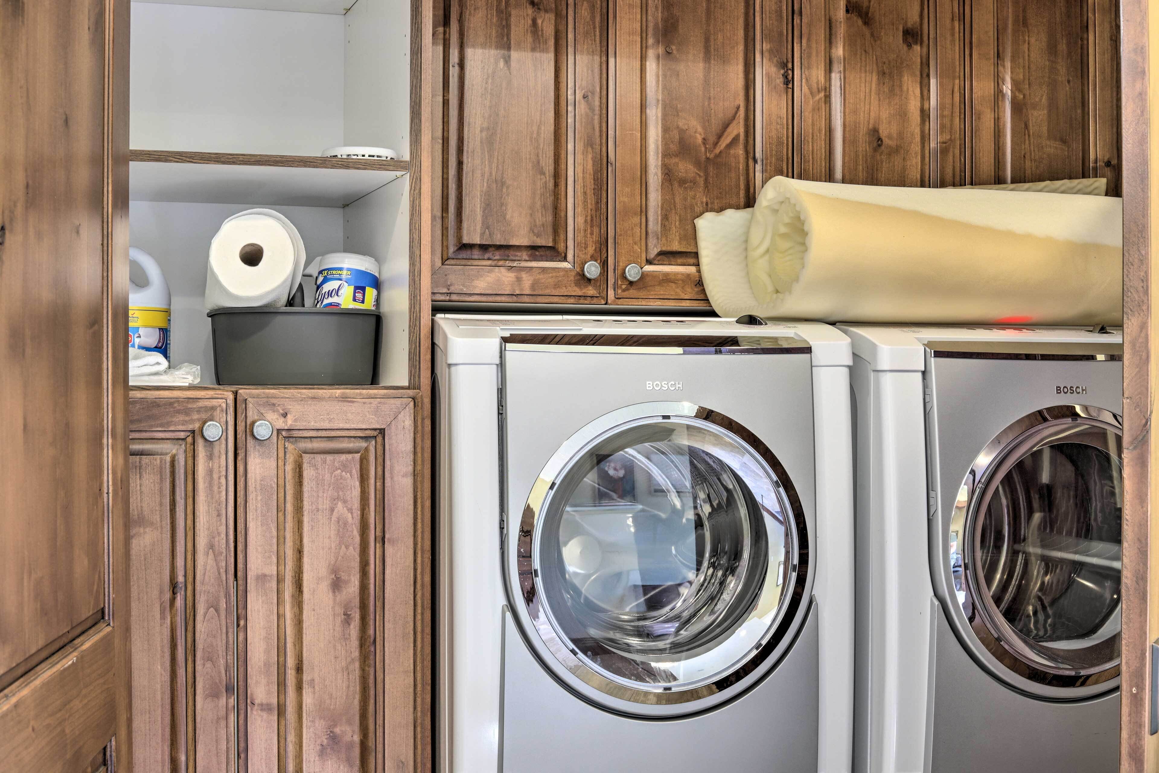 A laundry area with two Bosch washing machines, wooden cabinets, and a shelf with laundry supplies.