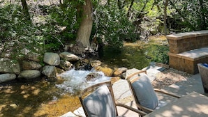 Un espace extérieur paisible, aménagé avec des sièges, où coule un petit ruisseau, le tout entouré de rochers et d’arbres.