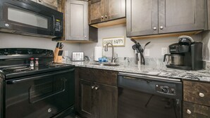 A kitchen with dark wooden cabinets, a black stove, a microwave, a coffee maker, and a sign that says "CHOOSE HAPPY".