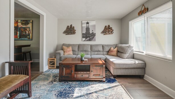 A living room with a sectional sofa, a wooden coffee table, and a large window with blinds.