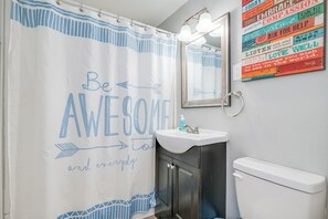 Un baño con cortina de ducha que dice "Be AWESOME and everyday", un lavabo, un espejo y un cartel motivacional en la pared.