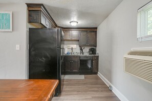 Una cocina compacta con armarios de madera oscura, un refrigerador negro y un horno empotrado.