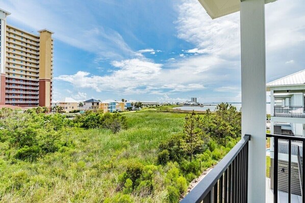 A balcony with a view of a grassy area, a tall building, and a body of water. - 1505 Sandpiper Ln | Private pool, beach/lagoon access! (Gulf Shores)