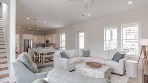A spacious living room with a white sofa set, a coffee table, and a dining area in the background. - 1505 Sandpiper Ln | Private pool, beach/lagoon access! (Gulf Shores)