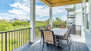 A covered outdoor patio with a table and chairs, overlooking a grassy area and buildings. - 1505 Sandpiper Ln | Private pool, beach/lagoon access! (Gulf Shores)
