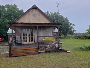 Situated in a grassy area, this cabin features a front porch with a bench and a small table.