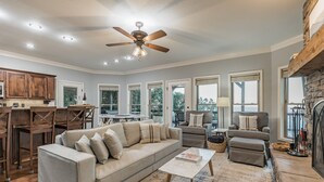 A spacious living room with a large sectional sofa, a coffee table, and a fireplace. There are multiple windows providing natural light and a view of the outdoors. - ON Mt Nebo State Park Luxury Mountain Retreat with Above the-clouds sunrise view (Dardanelle)