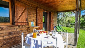 Una cabaña de madera con una mesa para dos, una terraza de madera y vistas del bosque circundante.