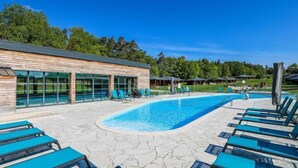Un área de piscina moderna con sillones reclinables, un edificio con amplias ventanas y un cielo azul despejado.