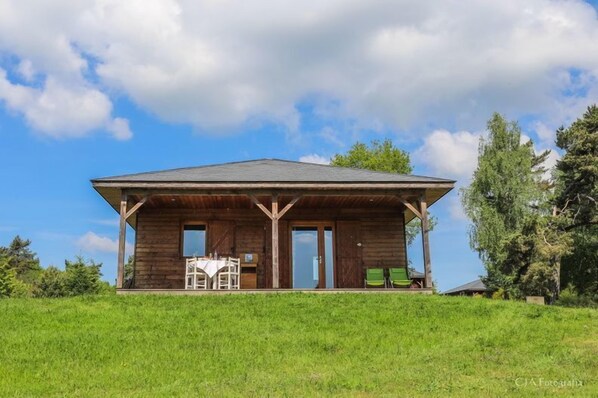 A wooden cabin with a flat roof, a covered porch, and a dining area with a table and chairs.