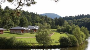Propiedad junto al lago con varias cabañas, una zona verde y un paisaje boscoso de fondo.