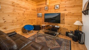 L’intérieur d’un chalet confortable en bois, avec un canapé en cuir, un fauteuil bleu, un téléviseur et une cheminée.