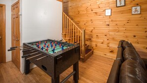 Une pièce avec une table de baby-foot, des murs en bois, un escalier et un canapé en cuir.