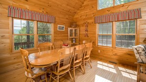 Une cabane en bois avec une table et des chaises, de grandes fenêtres et une vue sur l’extérieur.