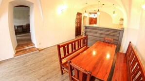 A dining area with a wooden table and benches, an arched doorway, and a kitchen with wooden cabinets and pendant lighting. - Beautiful 4 Bedroom apartment (Chvalsiny)