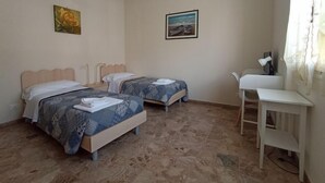 Une chambre avec deux lits, un bureau et une chaise. Il y a deux tableaux accrochés aux murs.