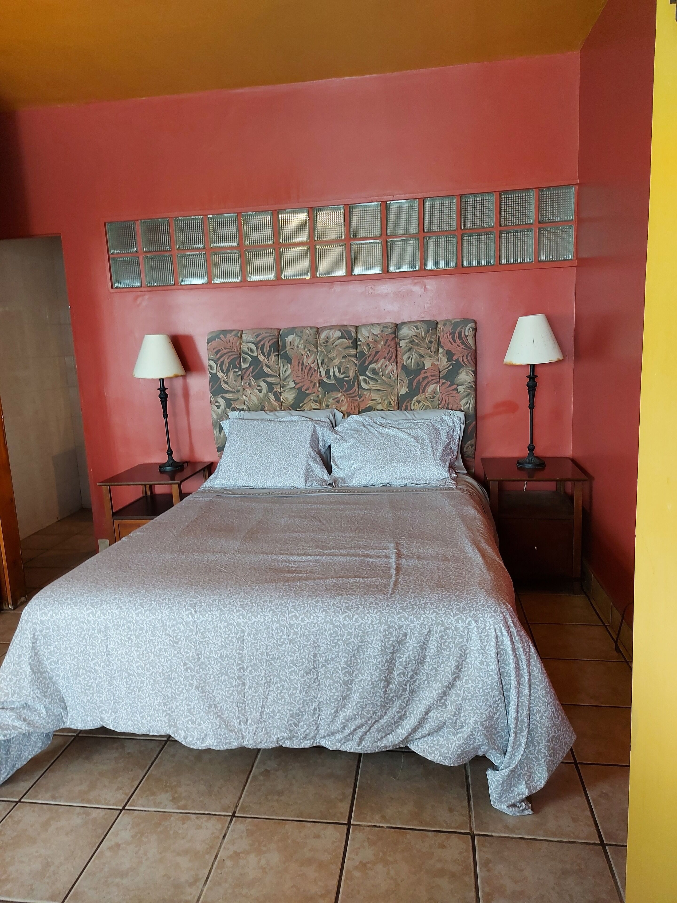 A bed with a patterned bedspread, two bedside tables with lamps, a decorative wall panel, and a tiled floor.