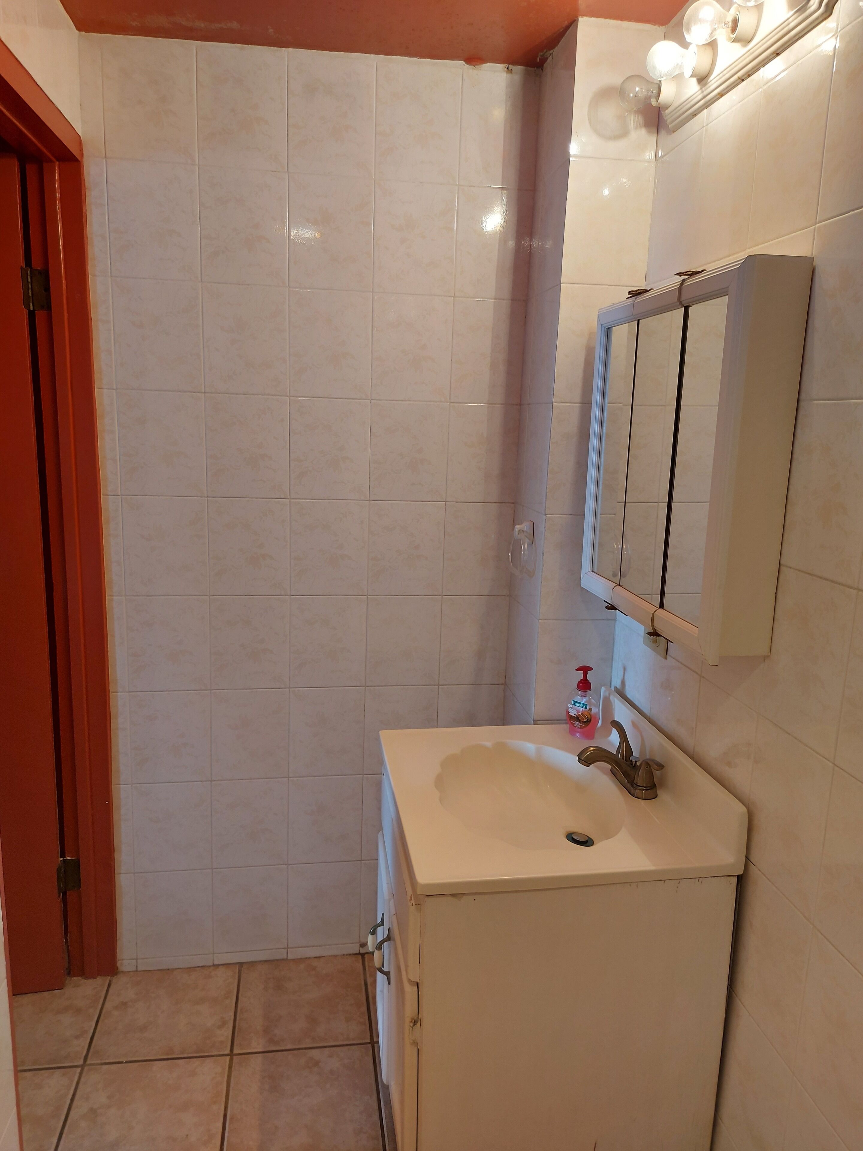 A bathroom with white tiles, a sink, a mirror, and a red door.