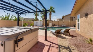 Un patio trasero con un jacuzzi, una piscina y sillas de descanso.