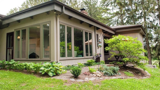 Een modern huis met grote ramen, een tuin met verschillende planten en een boom.