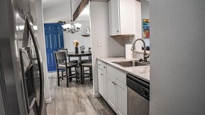A modern kitchen with white cabinets, a stainless steel refrigerator, and a dining area with a blue door.