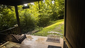 A wooden deck with a bench and a welcome mat, leading to a stone pathway surrounded by lush greenery.
