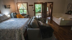 A cozy bedroom with a large bed, a sofa, a chair, and a view of the outdoors through a door.