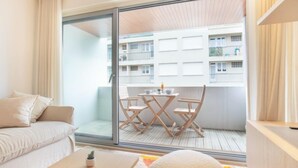 Une chambre d’hôtel moderne dotée d’un balcon, d’un canapé, d’une petite table et offrant une vue sur l’immeuble situé de l’autre côté de la rue.